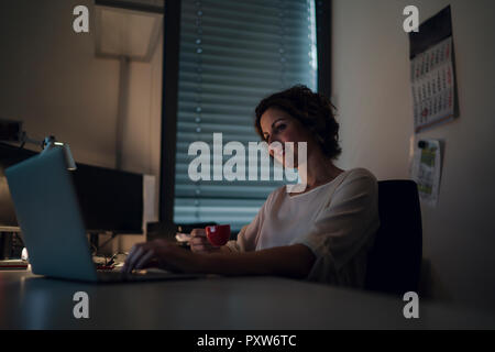 Businesswoman working overtime, using laptop, drinking coffee Stock Photo
