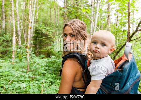 Portrait of smiling mother hiking in the woods with baby boy in backpack