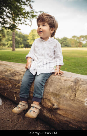 Happy toddler sitting on tree trunk in park Stock Photo