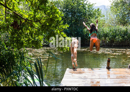 Two carefree girls jumping into pond