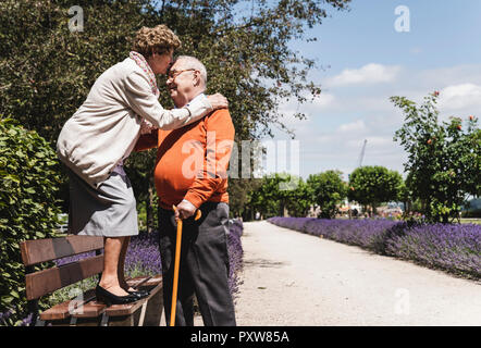 Senior couple having fun in the park, woman standing on bench kissing senior man on forehead Stock Photo