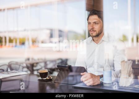 Businessman behind windowpane using tablet in a cafe Stock Photo