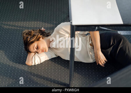 Tired businesswoman sleeping on floor under her desk Stock Photo