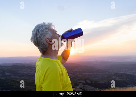 Spain, Catalonia, Montcau, senior man drinking water and looking at view from top of hill during sunset Stock Photo