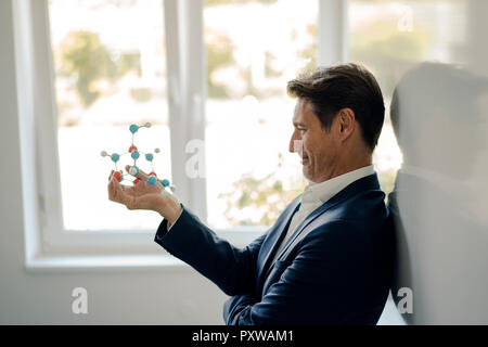 Successful businessman leaning on whiteboard, holding molecule model Stock Photo