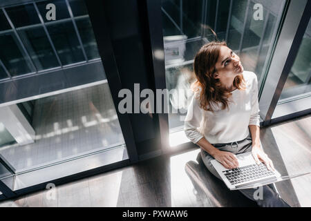 Businesswoman sitting on ground in empty office, using laptop Stock Photo