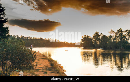 Sao Domingo Mine, Portugal - September 13, 2018:  Man fishing on the shores of the lake, at the end of the dirt road, with the orange sky and clouds i Stock Photo