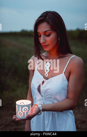 Young woman in nature, holding candle in the evening Stock Photo