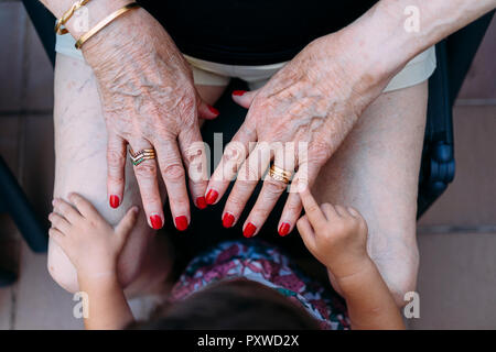 Hand of baby girl pointing on hand of senior woman with rings and red painted nails Stock Photo