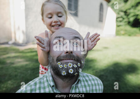 Portrait of mature man with daisies in his beard playing with little daughter in the garden Stock Photo