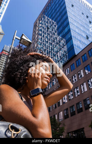 Germany, Frankfurt, portrait of young woman with smartwatch on the phone in front of skyscrapers Stock Photo