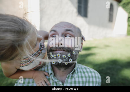 Portrait of smiling mature man with daisies in his beard playing with little daughter in the garden Stock Photo