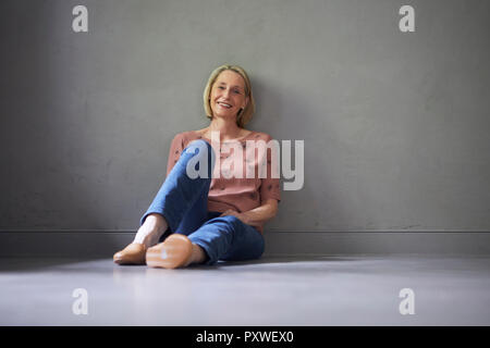 Portait of smiling mature woman at home sitting on the floor Stock Photo