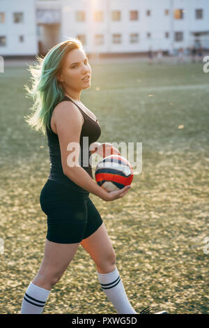 Young woman walking on football ground holding the ball Stock Photo