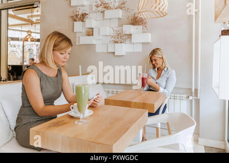Two young women using smartphones in a cafe Stock Photo