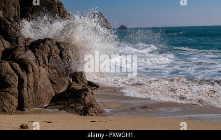 Sea swirling up the beach in waves crashing against the cliff rocks to shower water into the air in a white fountain of power. Stock Photo