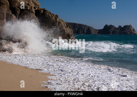 Sea swirling up the beach in waves crashing against the cliff rocks to shower water into the air in a white fountain of power. Stock Photo