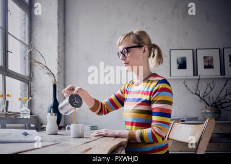 Woman pouring coffee in a mug at desk in a loft Stock Photo