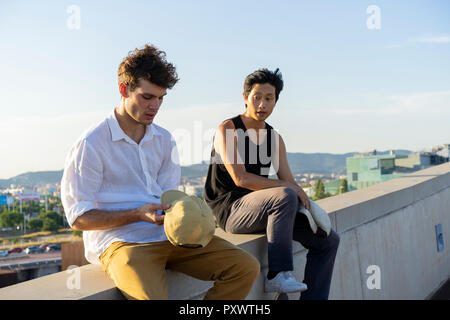 Two young men sitting and talking on a wall Stock Photo