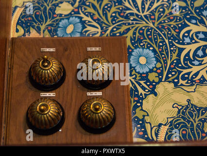 Four brass, domed vintage electrical light switches arranged in a square on bright wallpaper of blue and gold flowers and gold swirls at Lanhydrock. Stock Photo