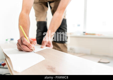Male worker applies markings to the Board for cutting with a electrofret saw. installing new wooden laminate flooring. concept of repair in house. Stock Photo