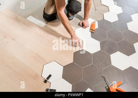 Male worker installing new wooden laminate flooring. The combination of wood panels of laminate and ceramic tiles in the form of honeycomb. Kitchen renovation. Stock Photo