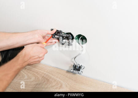 electrician connects the sockets to the electrical wires on wall in White room. Screwdriver, close-up electrician hands. Stock Photo