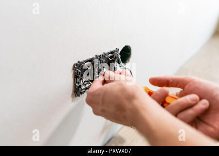 electrician connects the sockets to the electrical wires on wall in White room. Screwdriver, close-up electrician hands. Stock Photo
