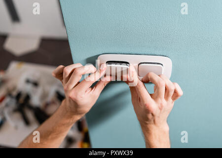 Electrician worker installs light switch and socket on wall in room. Screwdriver, close-up electrician hands. Stock Photo