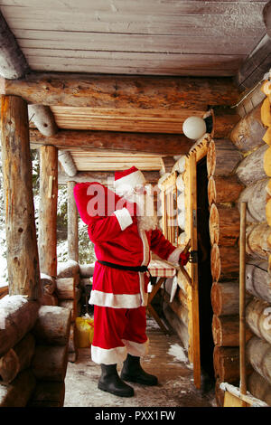 The real Santa Claus knocks on the door of the hut in the winter forest. Stock Photo