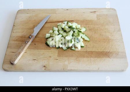 A wooden cutting board with a knife and some minced cucumbers on it, on a white surface Stock Photo