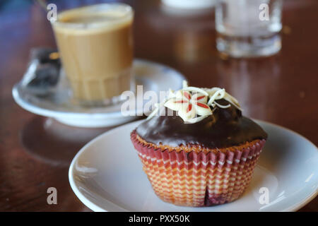 A close view of a chocolate muffin on a plate with a coffe cup on background (cafè con leche) on a table in Zaragoza, Spain Stock Photo