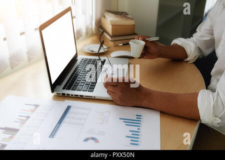 Business man use on-line via laptop computer for analyzing financial chart,writing business plan,open net-book and drinking a cup of coffee,morning li Stock Photo