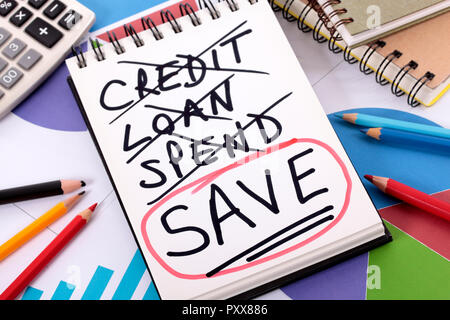 The word Save circled in red below a list of spending written on a notepad surrounded by pencils, graphs, books and calculator. Stock Photo