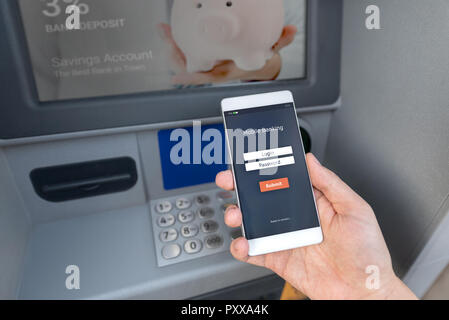Withdraw money from an ATM without using a credit card. Person holding a phone with a login screen for mobile banking. Stock Photo
