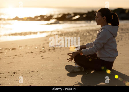 woman sitting crossed legged, meditating by the sea, lens flare Stock Photo