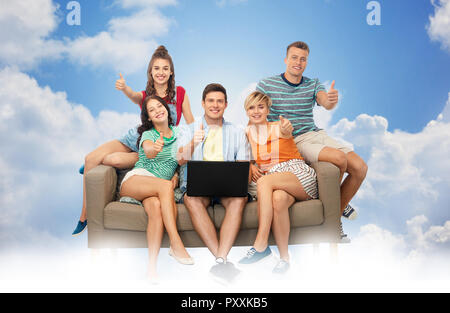 friends with laptop sit on sofa and show thumbs up Stock Photo
