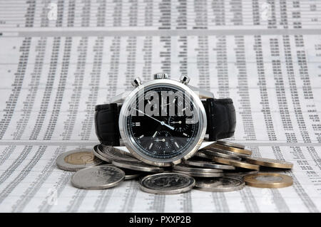 High class male watch lying on coins, stock market quotes in background Stock Photo