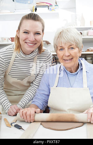 Portrait Of Senior Woman Rolling Out Clay With Teacher In Pottery Class Stock Photo