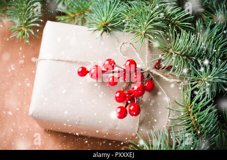 Wrapped christmas presents, fur tree branches, red berries on rustic wooden background. Drawn snow effect. Place for text. Selective focus. Stock Photo