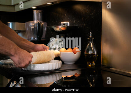 Arms of male chef using rolling pin to roll out pastry into a dish Stock Photo