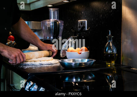 Arms of male chef using rolling pin to roll out pastry into a dish Stock Photo