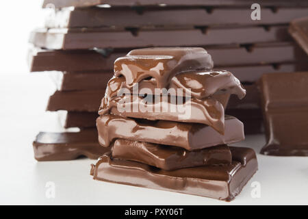 Stack of melting chocolate's pieces with big stack of chocolate on background on white background Stock Photo