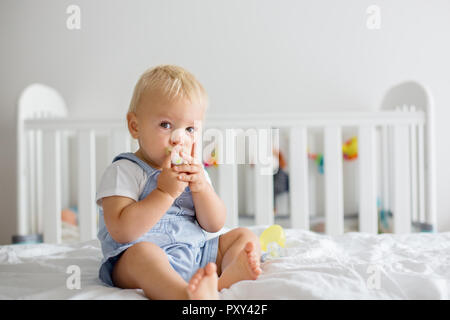 Toddler baby boy, playing with dummy, crying unhappy for the pacifier in children bedroom Stock Photo