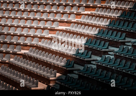 Free unclaimed seats in multiple rows. Sunset photo in empty public arena and concert amphitheatre. Red brick and white travertine structure. Stock Photo