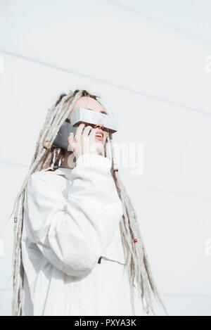 Young woman talking on smartphone in futuristic clothes and shades Stock Photo
