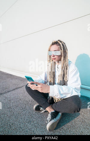 Young woman looking at smartphone in futuristic clothes and shades Stock Photo