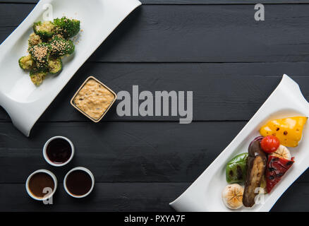 salads, vegetable food and sauces in plates on a black wooden background Stock Photo