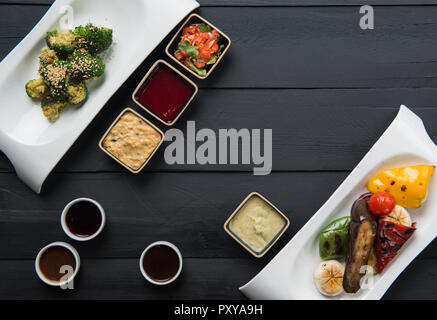 salads, vegetable food and sauces in plates on a black wooden background Stock Photo