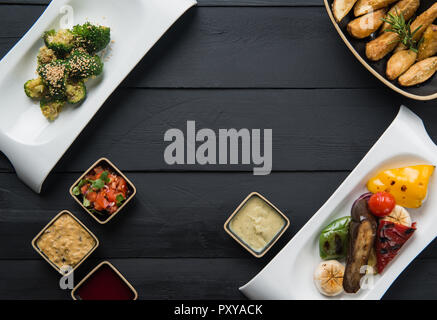 salads, vegetable food and gravy in plates on a black wooden background Stock Photo